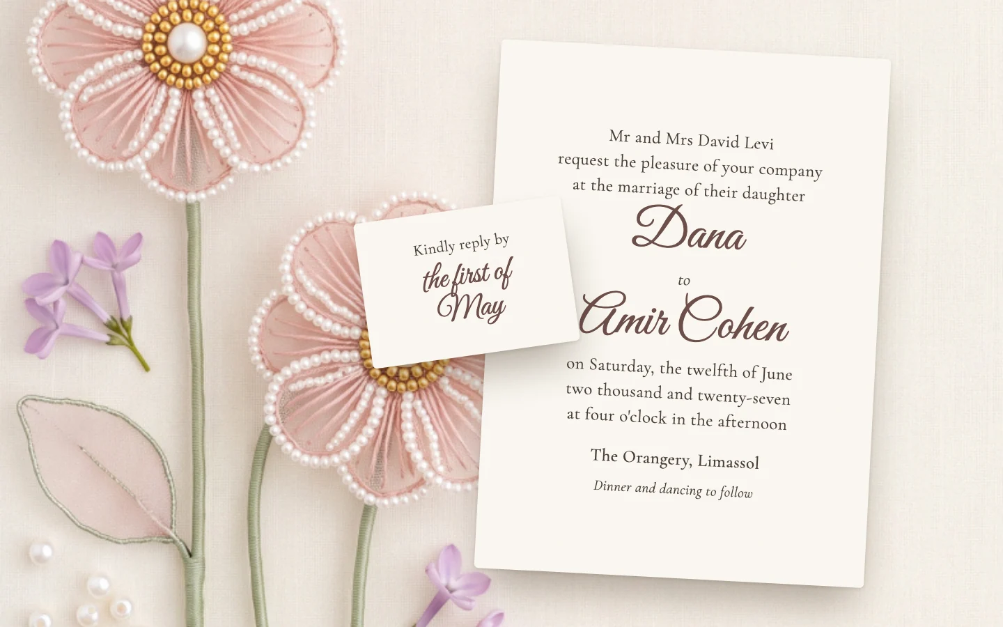 A printed wedding invitation with its wording set in serif and script, on cream linen beside pink sugar roses
