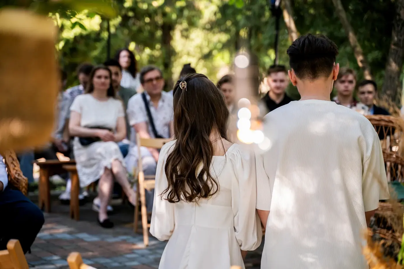 Guests seated at an outdoor wedding ceremony in a garden, watching the couple from behind